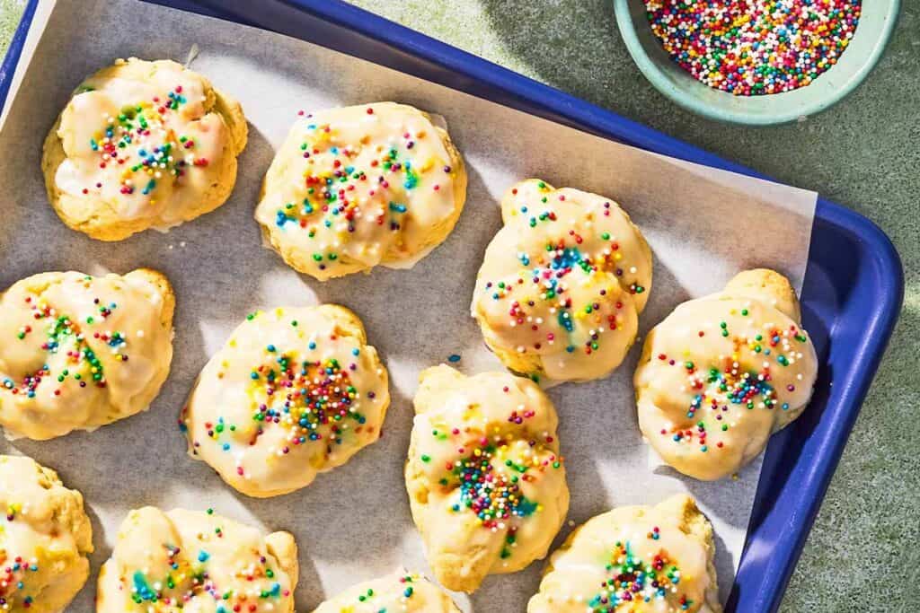 Italian lemon cookies on a parchment lined sheet pan next to a bowl of non-pareils.