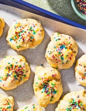Italian lemon cookies on a parchment lined sheet pan next to a bowl of non-pareils.