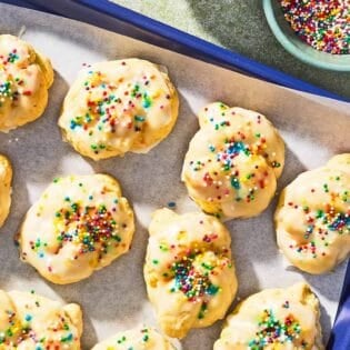 Italian lemon cookies on a parchment lined sheet pan next to a bowl of non-pareils.