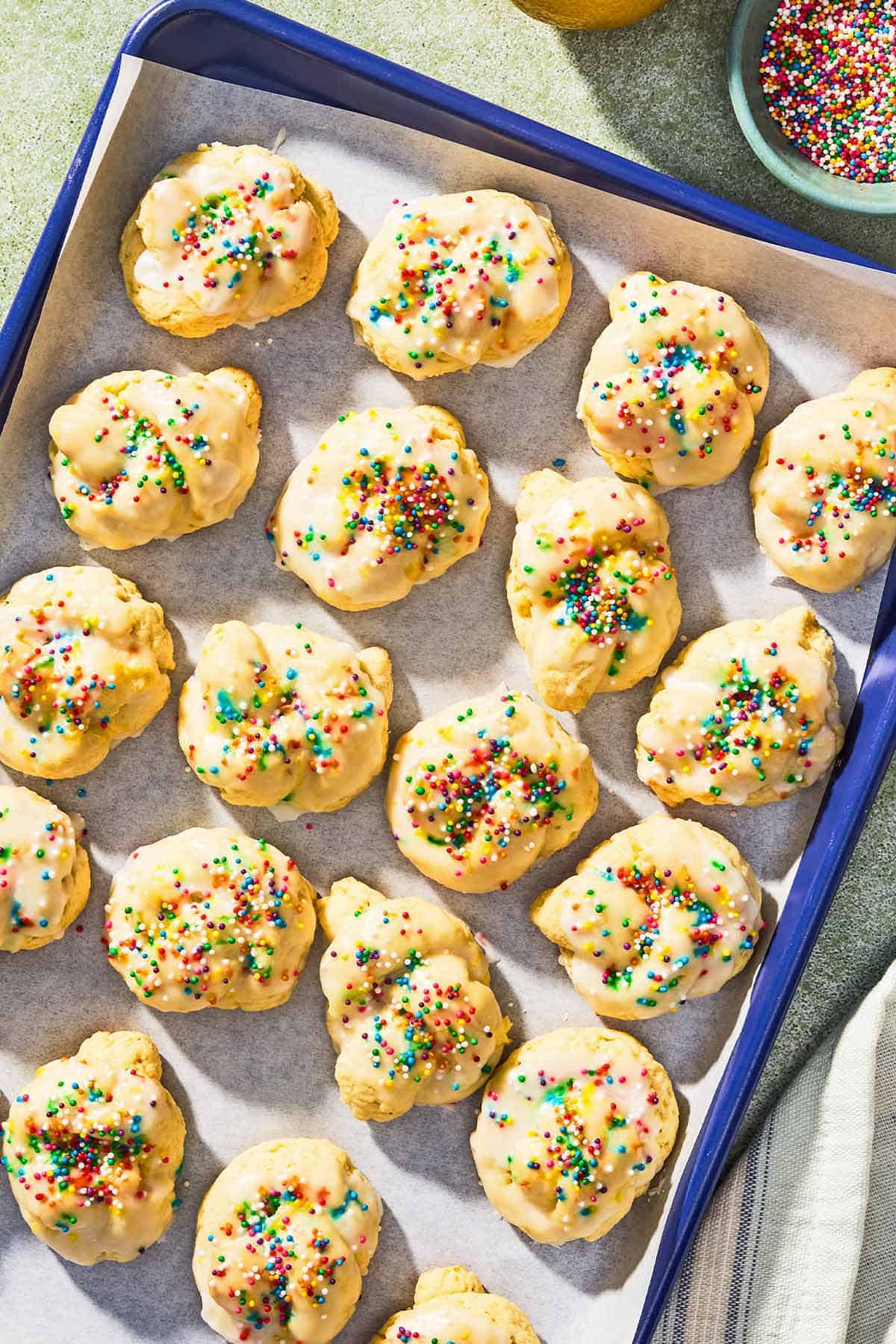 Italian lemon cookies on a parchment lined sheet pan next to a bowl of non-pareils.