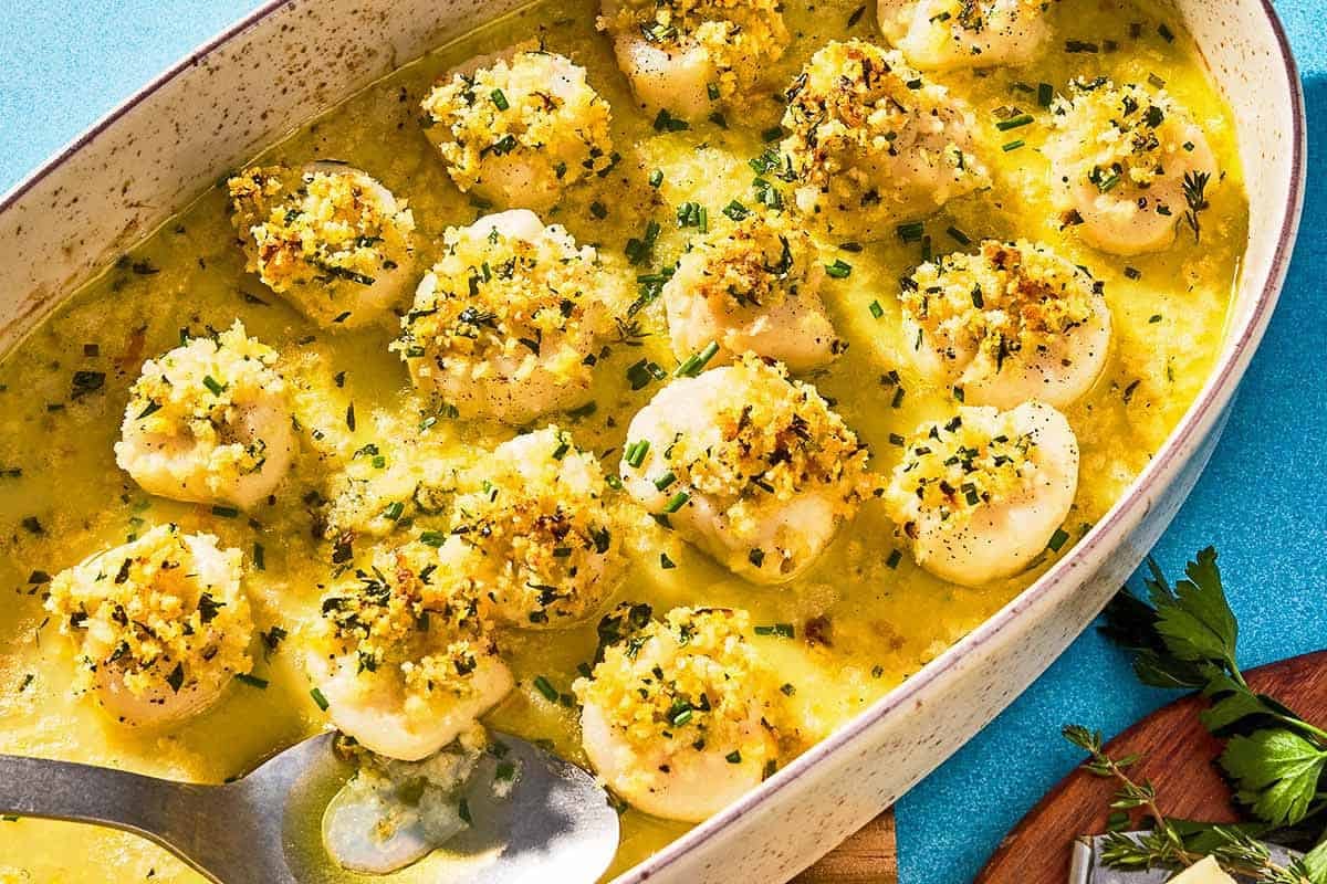 Baked scallops in a baking dish with a serving spoon.