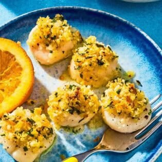 Five baked scallops on a plate with a fork and a lemon wedge.