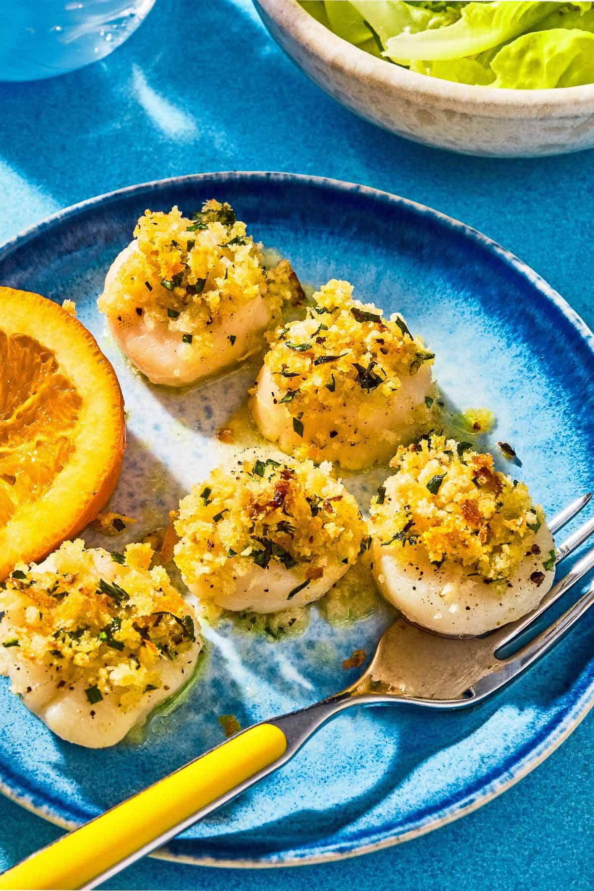 Five baked scallops on a plate with a fork and a lemon wedge.