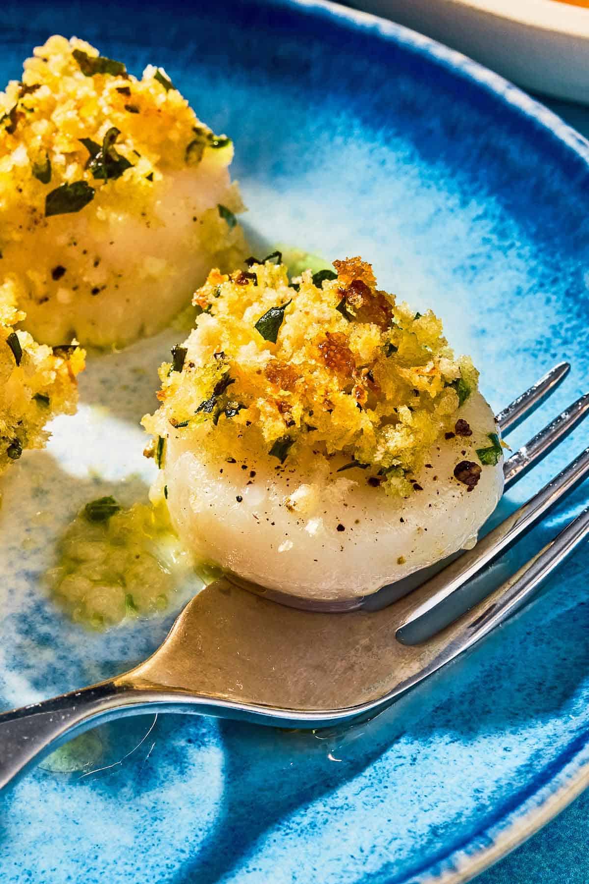 A close up of a baked scallop on a plate with a fork.
