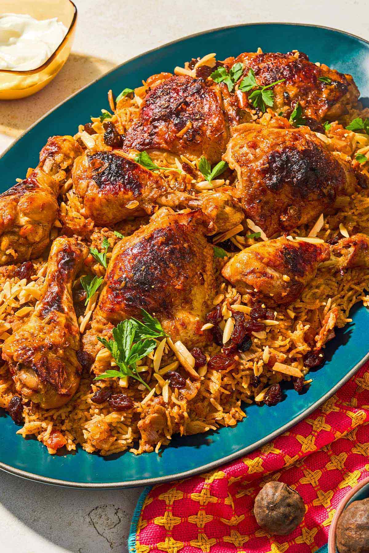 Kabsa on a platter topped with parsley next to a bowl of yogurt.