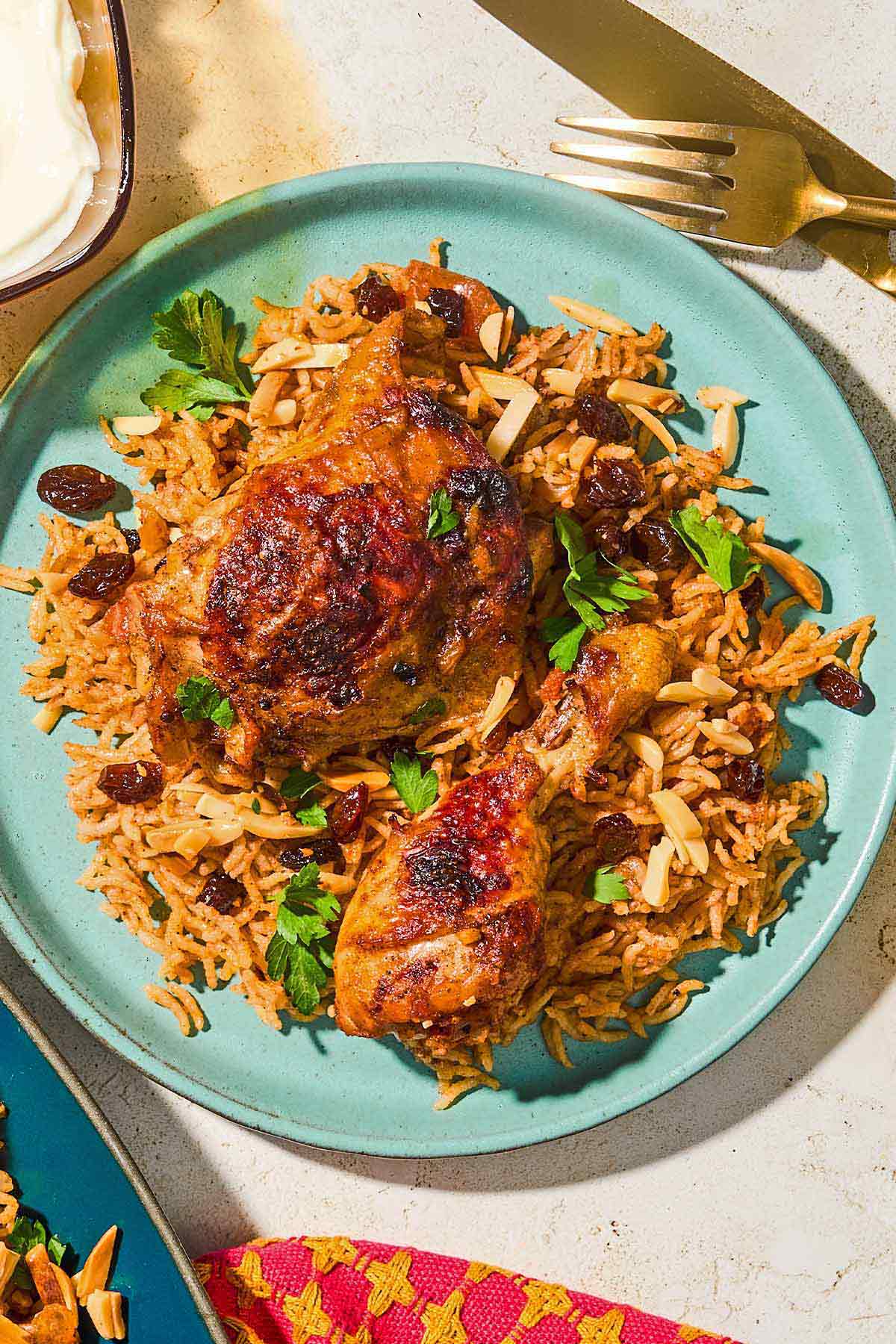 A serving of kabsa on a plate next to a knife and fork.