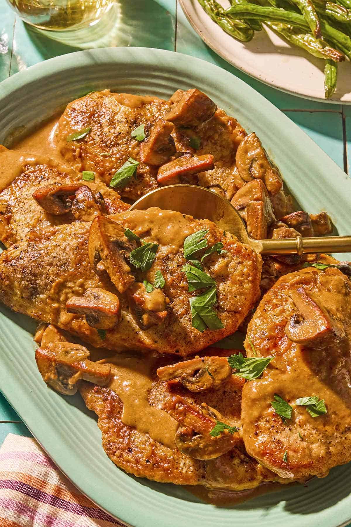Chicken marsala on a platter with a serving spoon next to a plate of green beans.