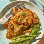Chicken marsala on a plate with green beans and a fork.