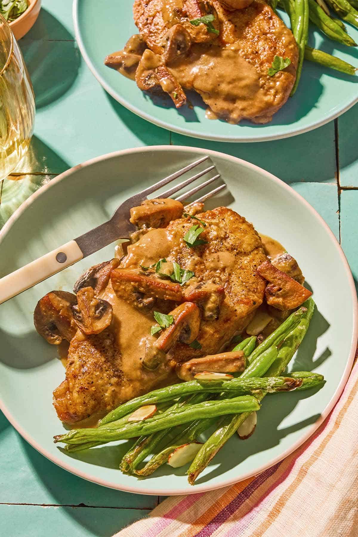 Two servings of chicken marsala on plates with green beans. One also has a fork.