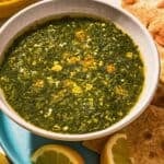 A bowl of molokhia in a bowl on a plate with pita and lemon wedges.