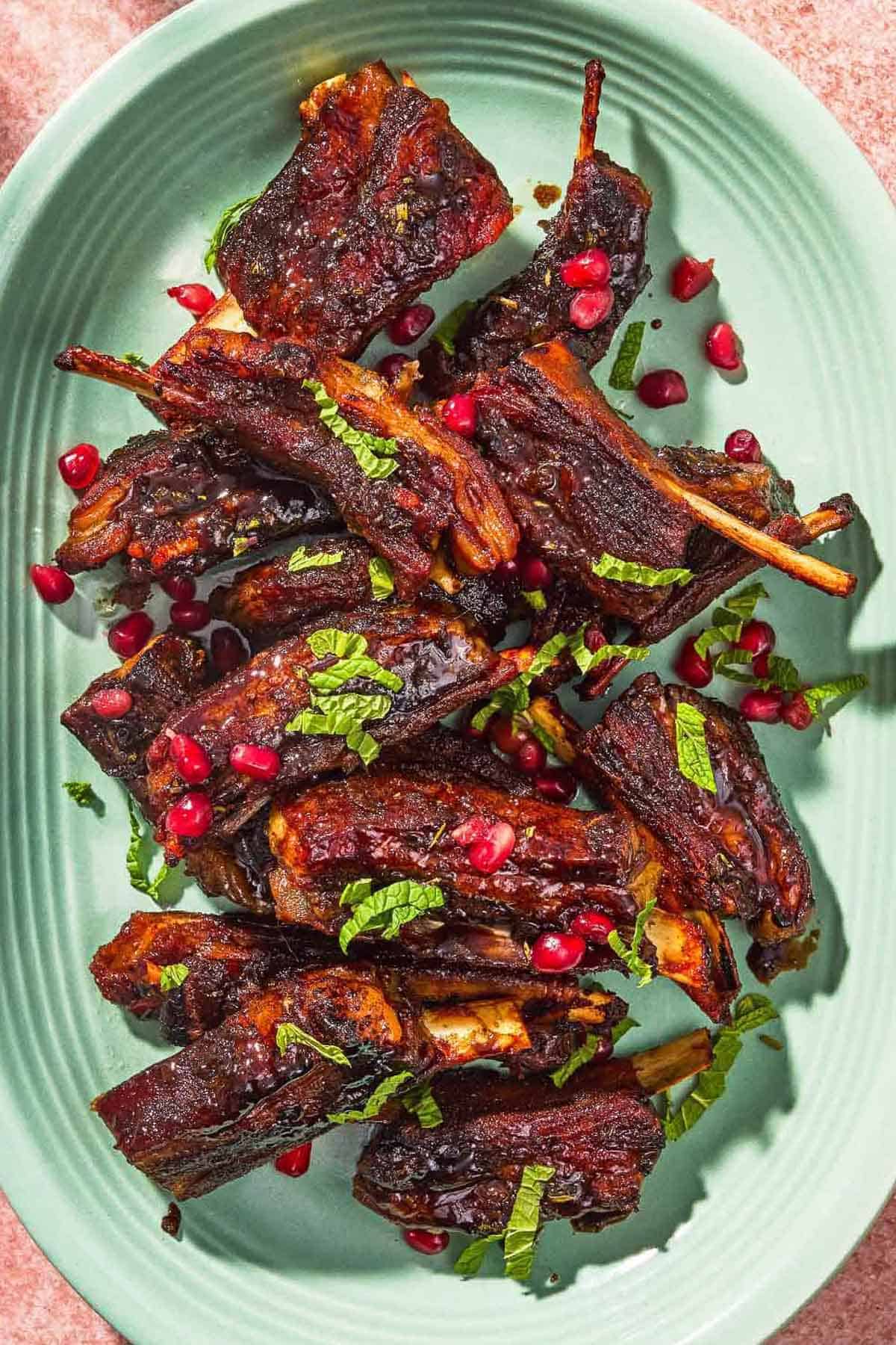 Mint green platter of lamb ribs garnished with fresh mint and pomegranate seeds.