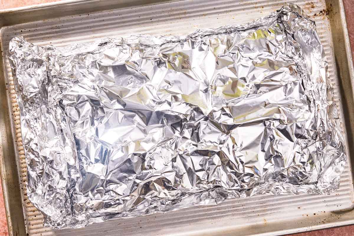 The lamb ribs wrapped in foil on a sheet pan.