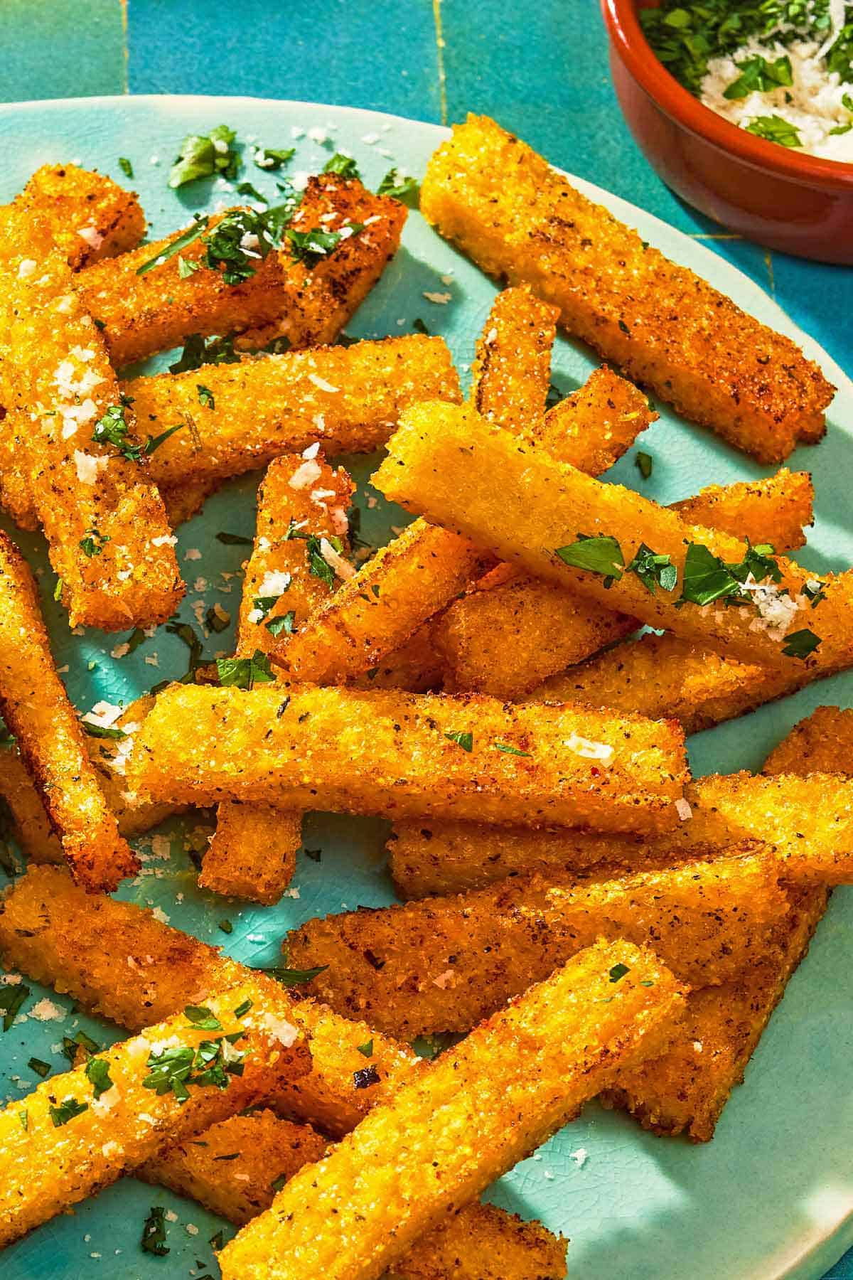 Polenta fries topped with grated parmesan cheese and parsley on a platter.