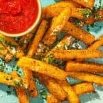 Polenta fries topped with grated parmesan cheese and parsley on a platter with a bowl of marinara sauce.