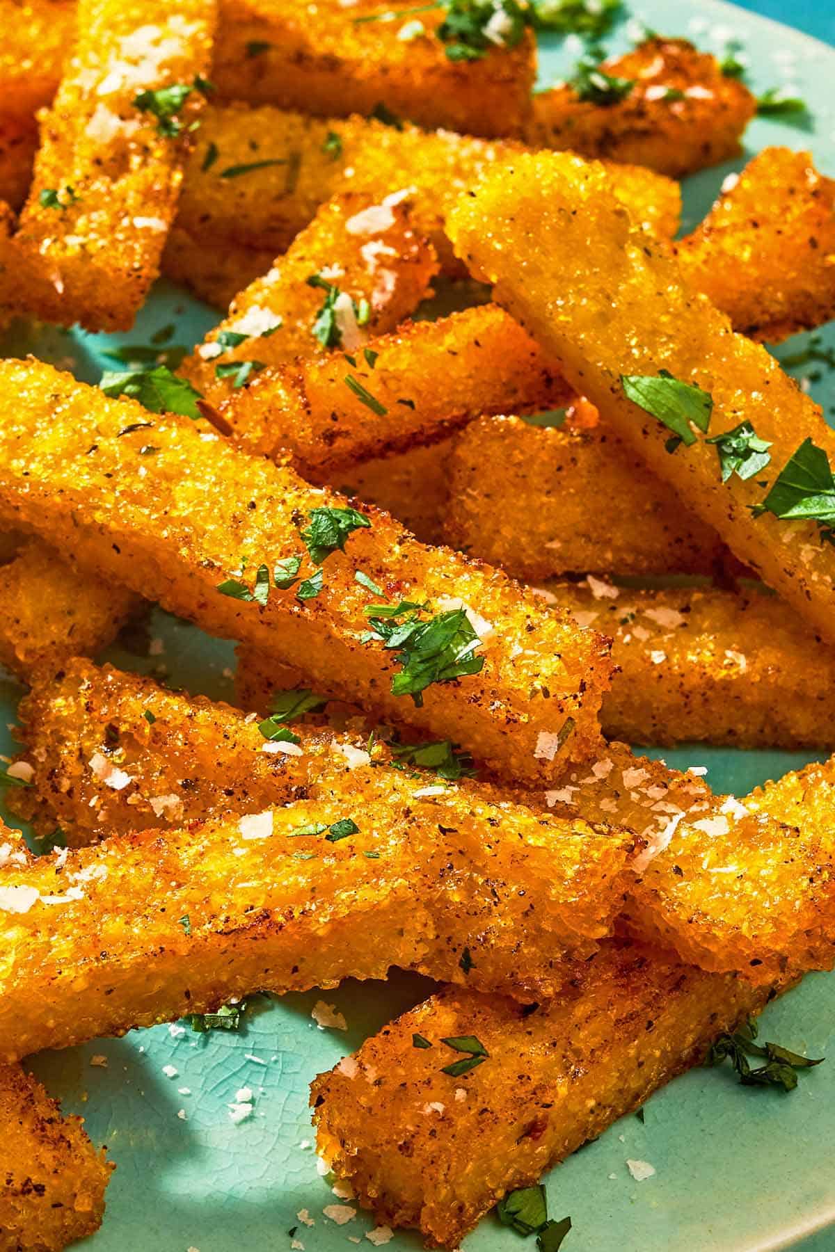 Polenta fries topped with grated parmesan cheese and parsley on a platter.