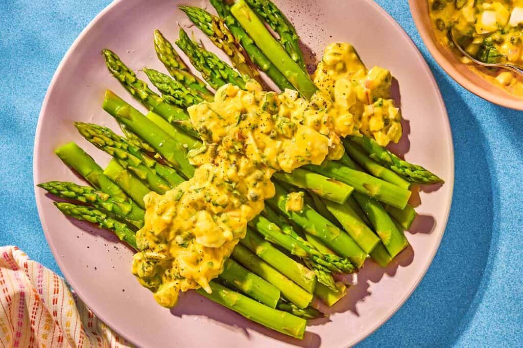 Sauce gribiche over asparagus on a plate.