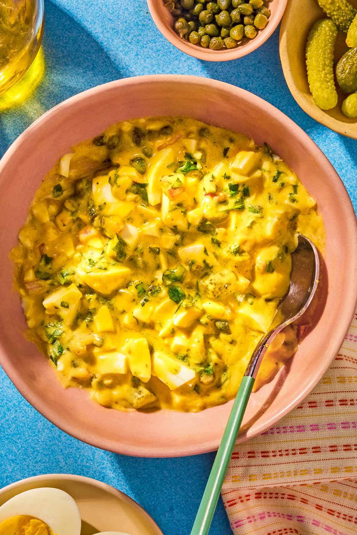 Sauce gribiche in a bowl with a spoon next to bowls of capers and gherkins.