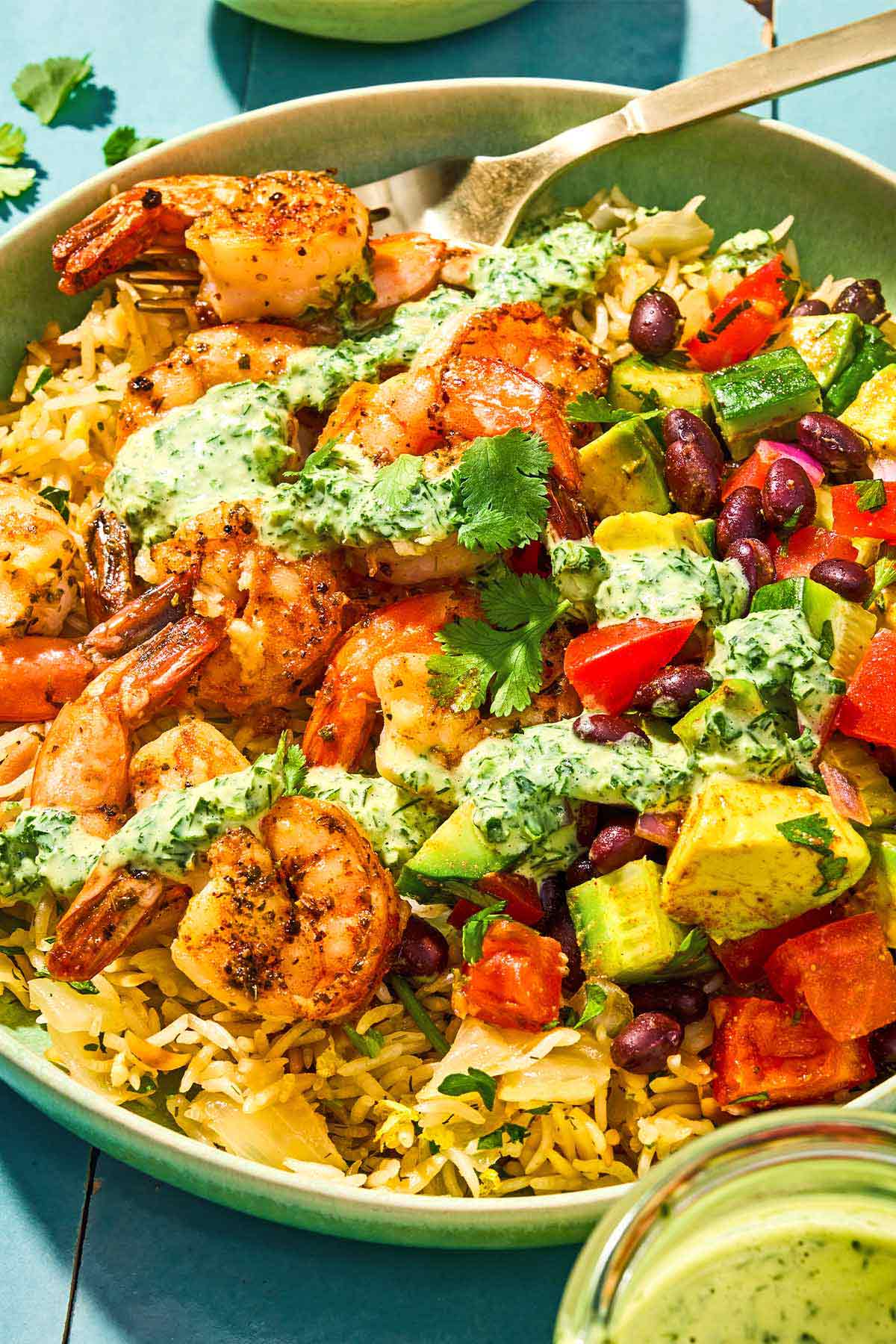 A shrimp bowl with a fork next to a jar of green goddess dressing.