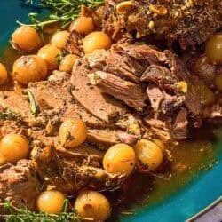 The sliced boneless leg of lamb with fresh herbs and pearl onions on a platter.