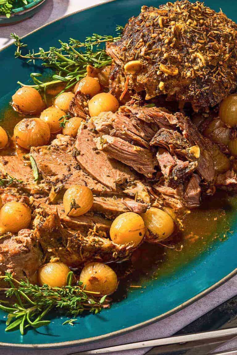 The sliced boneless leg of lamb with fresh herbs and pearl onions on a platter.