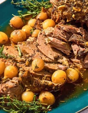 The sliced boneless leg of lamb with fresh herbs and pearl onions on a platter.