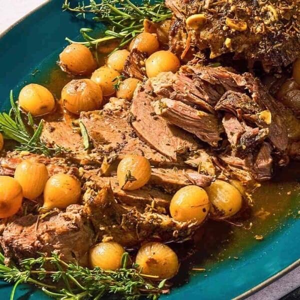 The sliced boneless leg of lamb with fresh herbs and pearl onions on a platter.