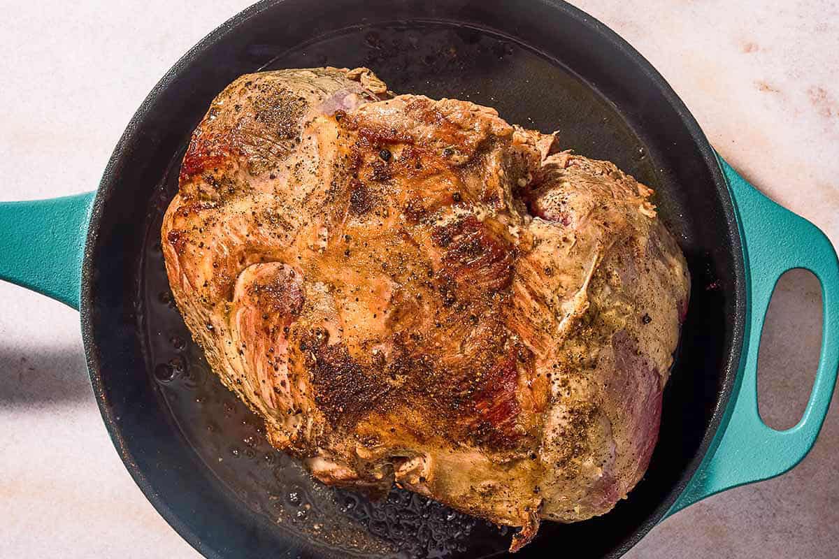The boneless leg of lamb being seared in a skillet.
