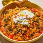 The swiss chard recipe topped with yogurt and olive oil in a serving bowl with a wooden spoon next to a bottle of olive oil.