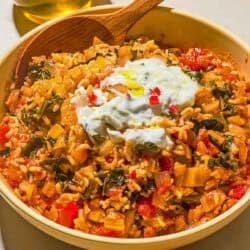 The swiss chard recipe topped with yogurt and olive oil in a serving bowl with a wooden spoon next to a bottle of olive oil.