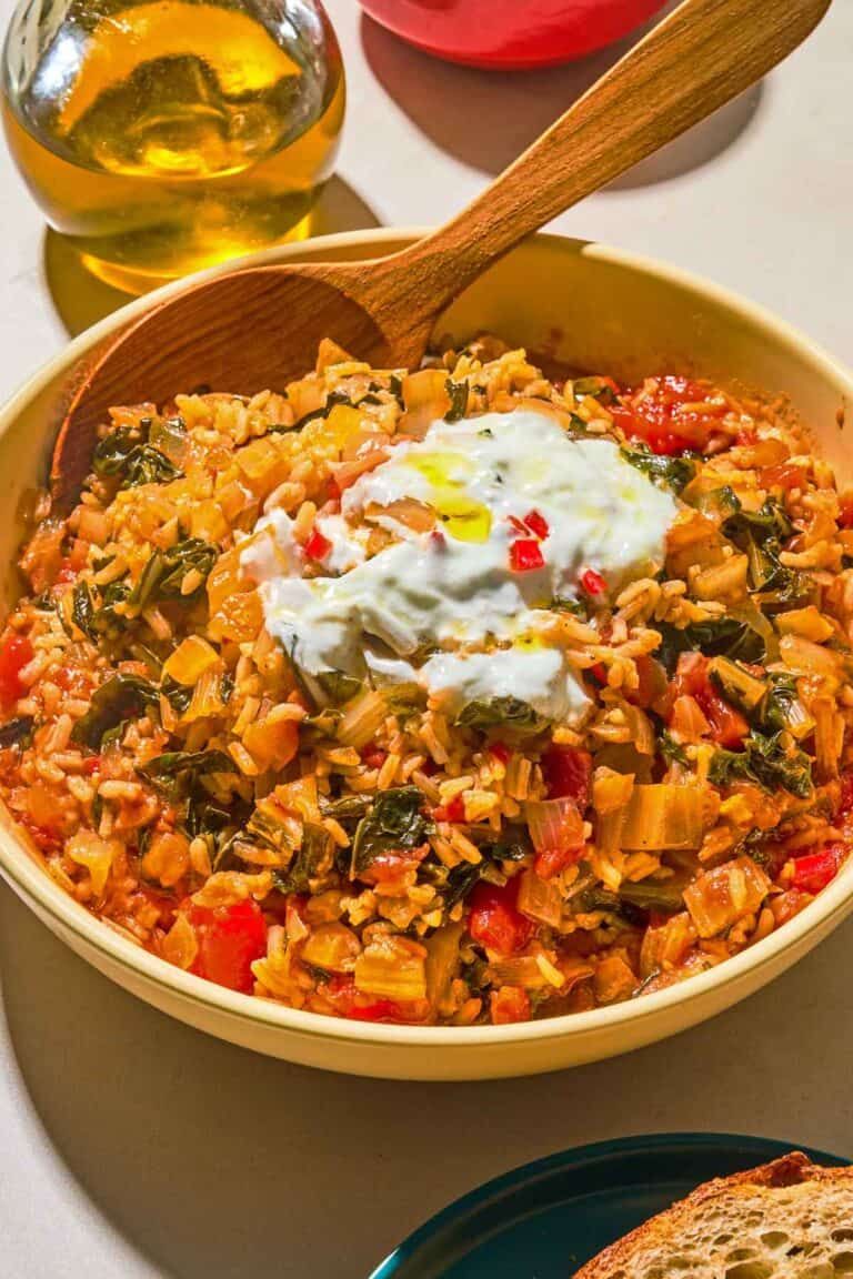 The swiss chard recipe topped with yogurt and olive oil in a serving bowl with a wooden spoon next to a bottle of olive oil.