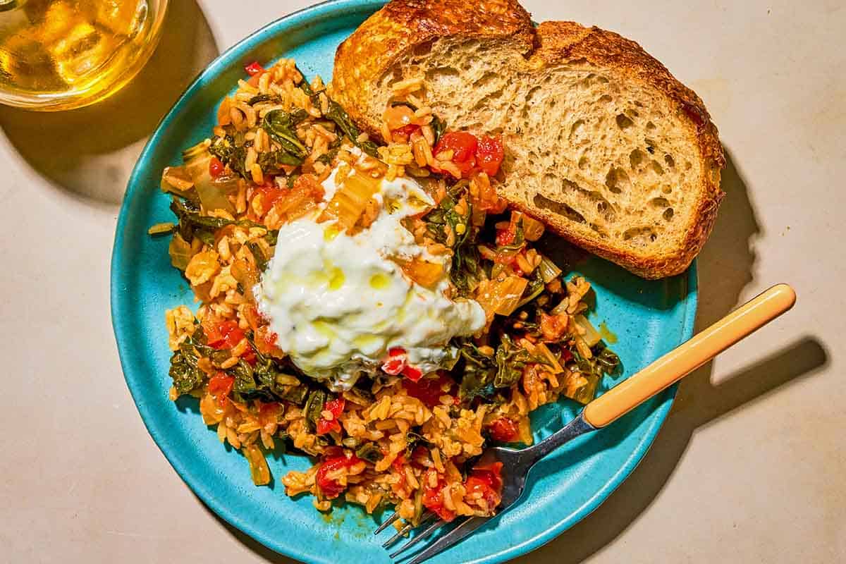 A serving of the swiss chard topped with yogurt and olive oil on a plate with a slice of bread and a fork.