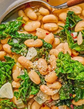 A close up of beans and greens in a bowl with a spoon.