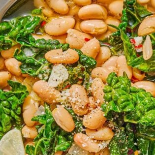 A close up of beans and greens in a bowl with a spoon.