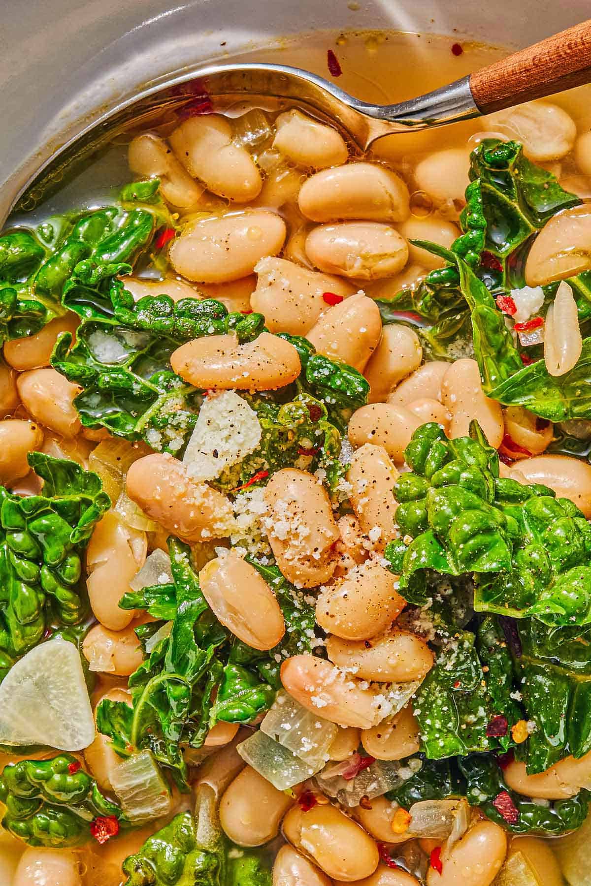 A close up of beans and greens in a bowl with a spoon.
