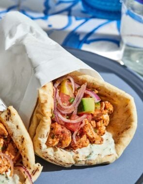 The doner kebab recipe with the cucumber tomato salad and tahini sauce on pita wrapped in a piece of parchment paper on a plate.