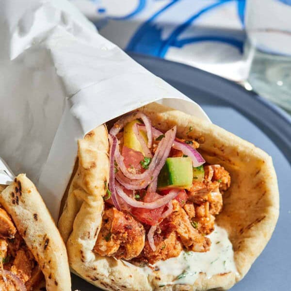 The doner kebab recipe with the cucumber tomato salad and tahini sauce on pita wrapped in a piece of parchment paper on a plate.