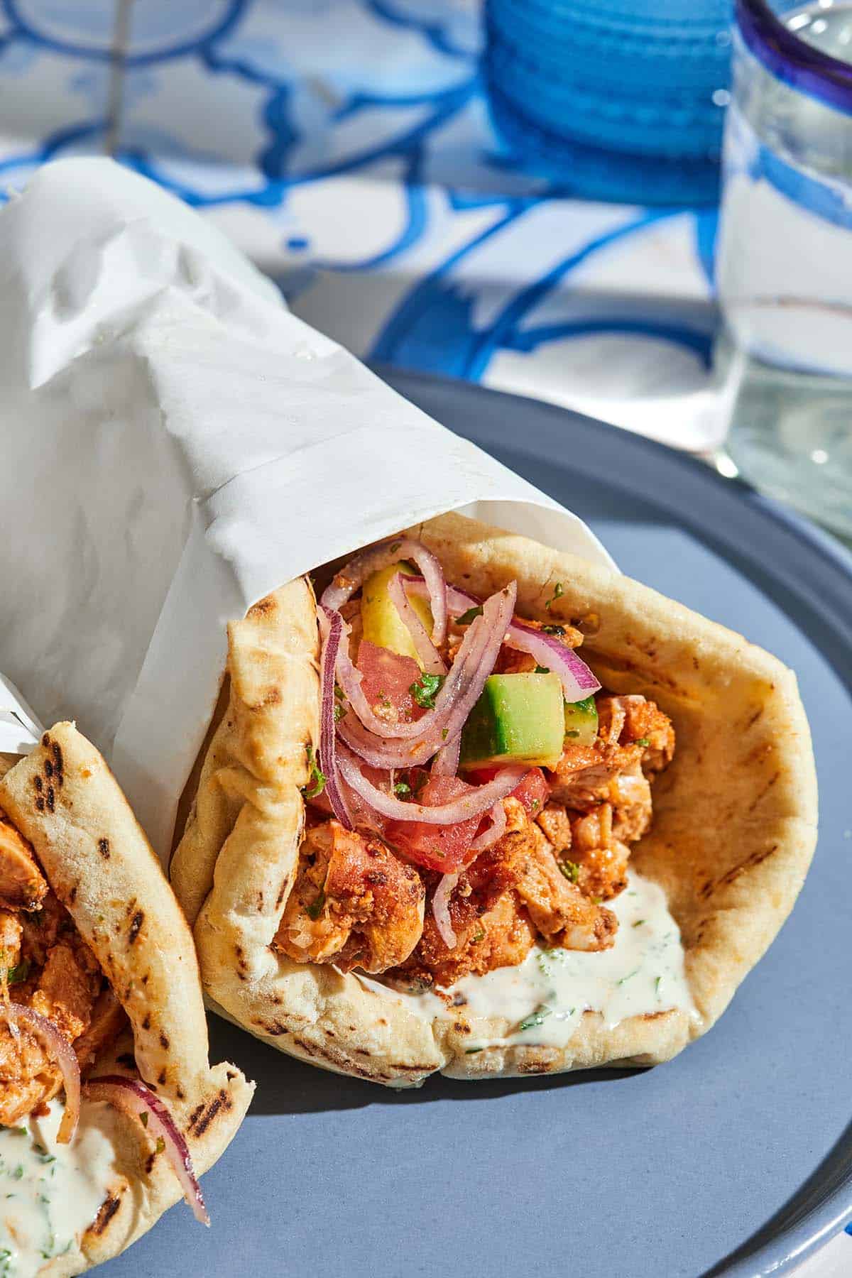 The doner kebab recipe with the cucumber tomato salad and tahini sauce on pita wrapped in a piece of parchment paper on a plate.