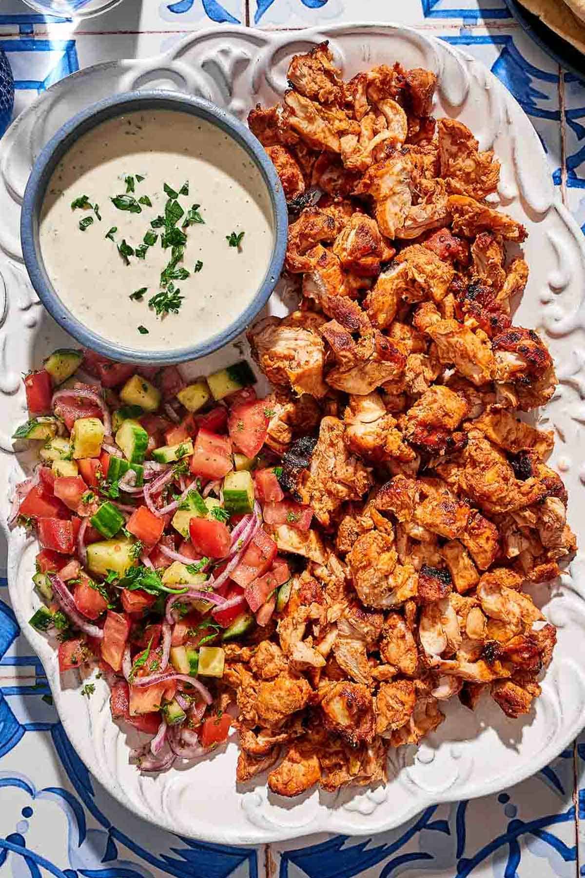 The doner kebab recipe on a platter with a salad and a bowl of tahini sauce.