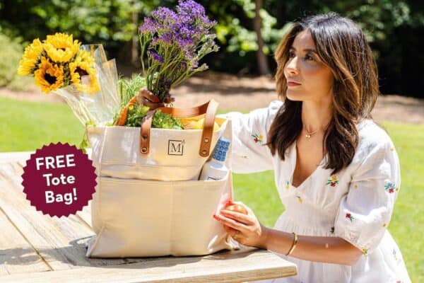 Suzy Karadsheh sitting outdoors at a picnic table with a tote bag filled with fresh flowers.