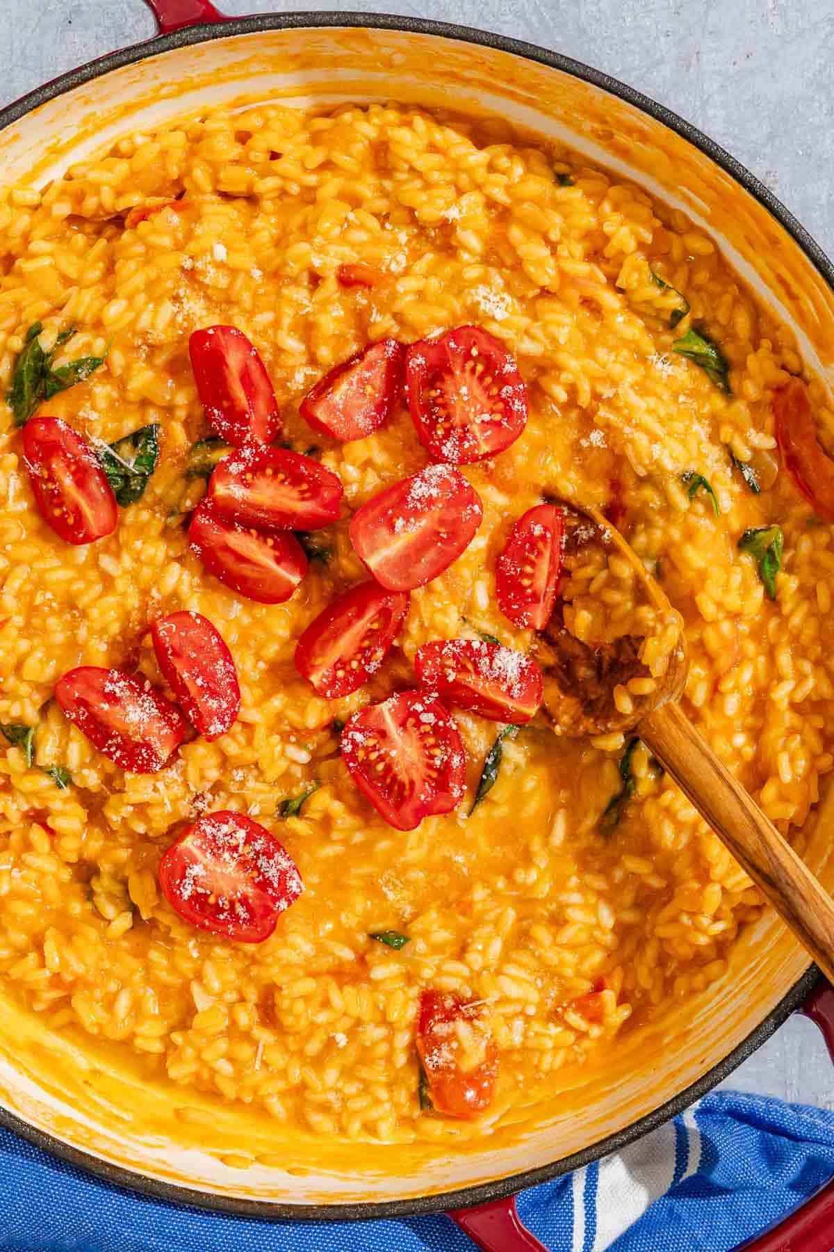 The tomato risotto in a pan with a wooden spoon.