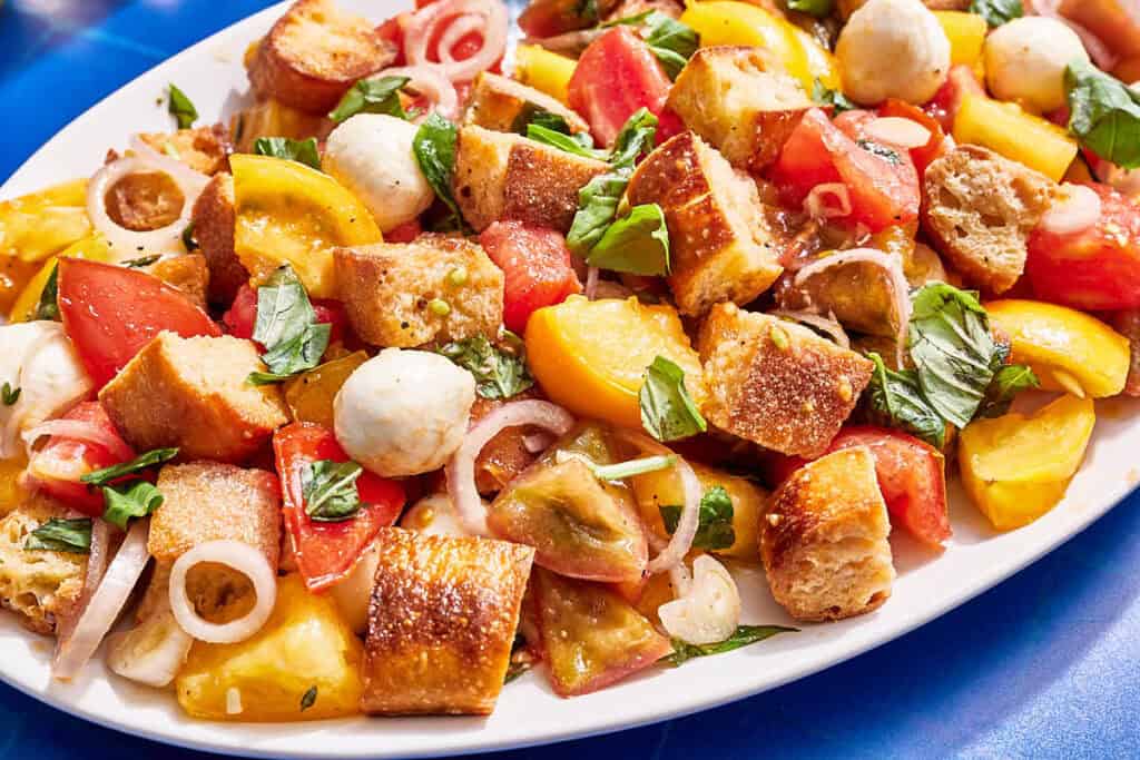 Panzanella salad on a serving platter with serving utensils.