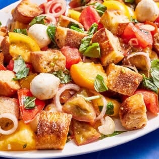 Panzanella salad on a serving platter with serving utensils.