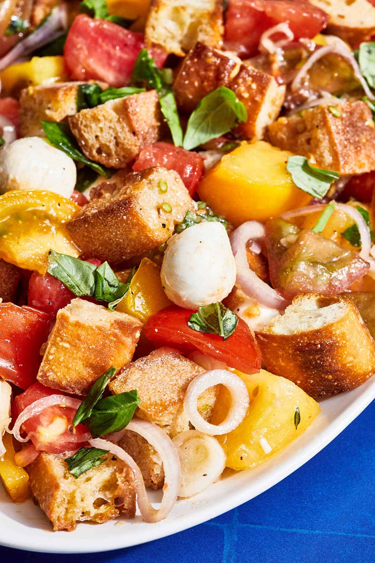 Panzanella salad with yellow and red tomatoes on a serving platter set against a blue background.