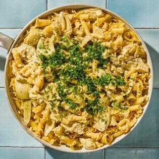 Artichoke pasta in a skillet topped with herbs.