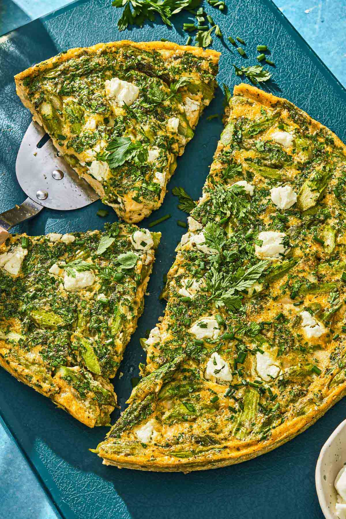 An asparagus frittata, half sliced into pieces on a cutting board.