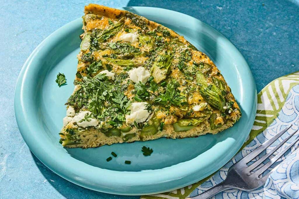 A slice of the asparagus frittata on a plate next to a fork.