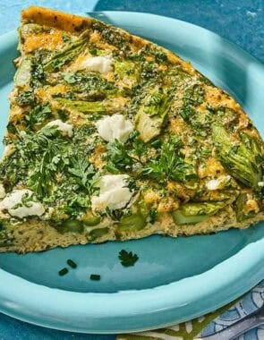 A slice of the asparagus frittata on a plate next to a fork.