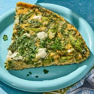 A slice of the asparagus frittata on a plate next to a fork.