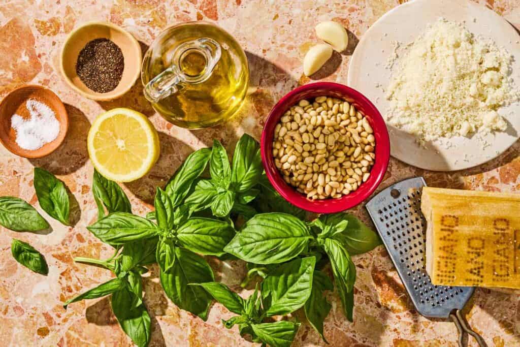 Ingredients for the basil pesto recipe including basil, garlic, pine nuts, olive oil, lemon, grated parmesan cheese, salt and black pepper.