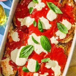 The eggplant parmesan recipe in a baking dish next to a bowl of grated parmesan.